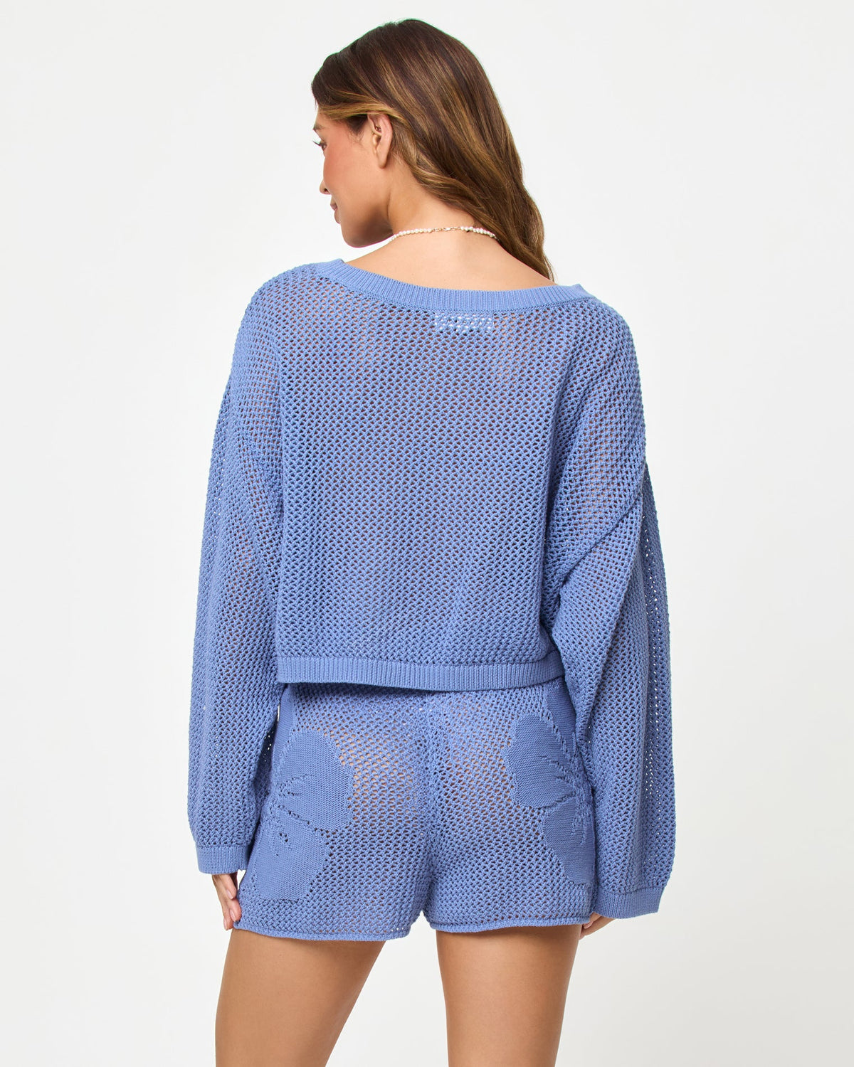 Back view of a model wearing the LSPACE Island Time Sweater in Chambray, styled with the matching Island Time Short, showing the open-knit crochet construction and relaxed fit.