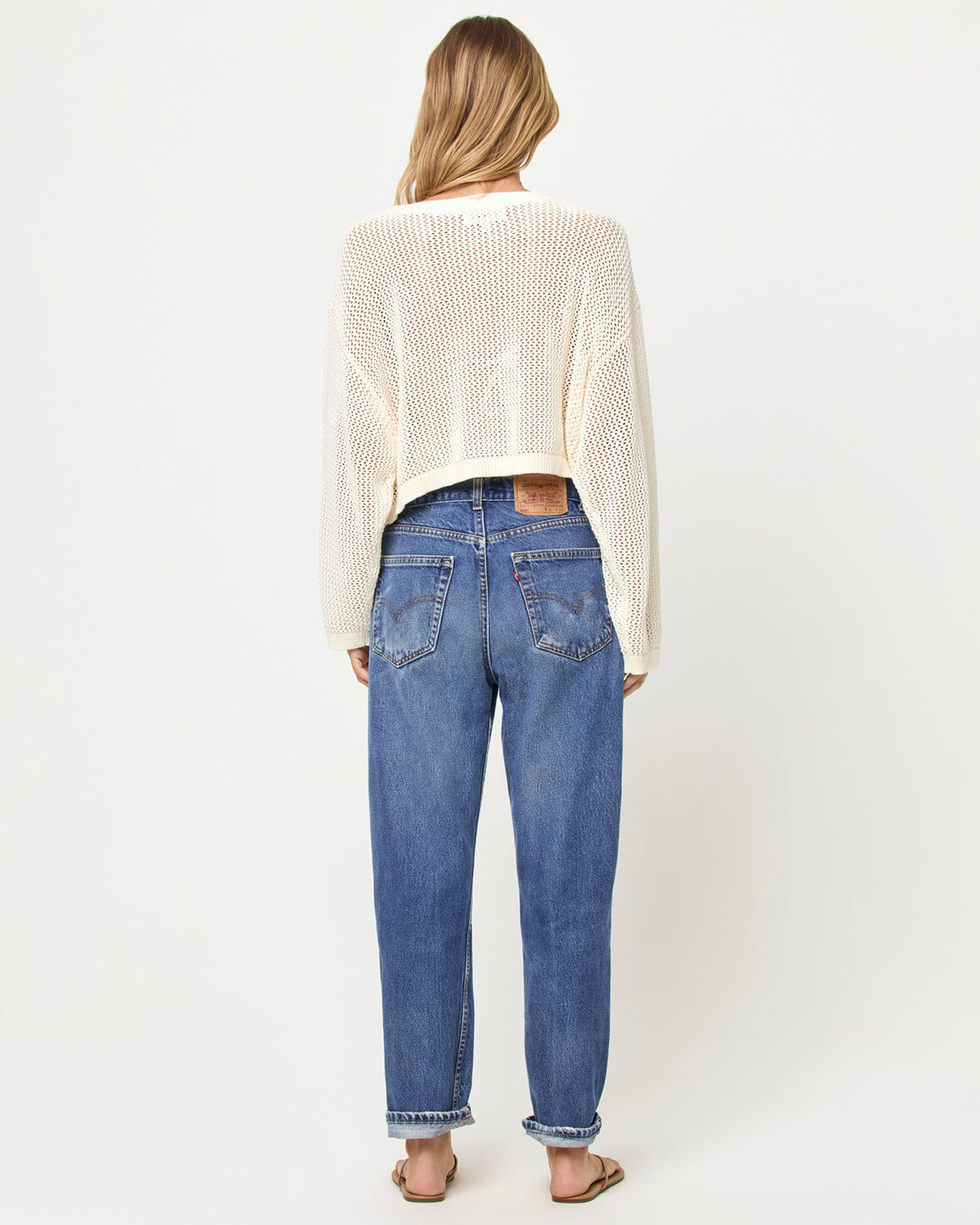 Back view of a model wearing the LSPACE Island Time Sweater in Cream, styled with jeans, showing the open-knit crochet construction and relaxed fit.