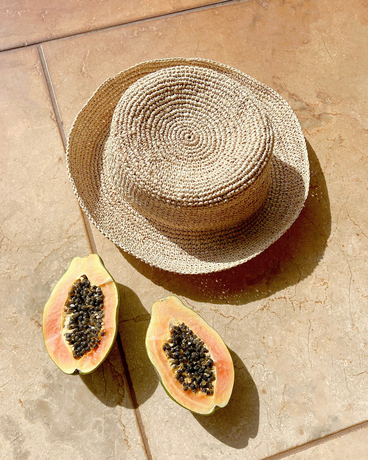 Flat lay of the Isadora Bucket Hat in natural styled with tropical fruits on a terracotta tile.